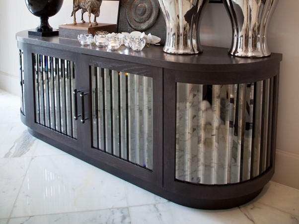 This media sideboard features a long rectangular shape with curved ends and a smooth top wood surface, the main storage unit is crafted from wood veneer and glass. Stylish mirror doors fitted with handles are added to provide contrast against the gorgeous dark walnut colour wood.