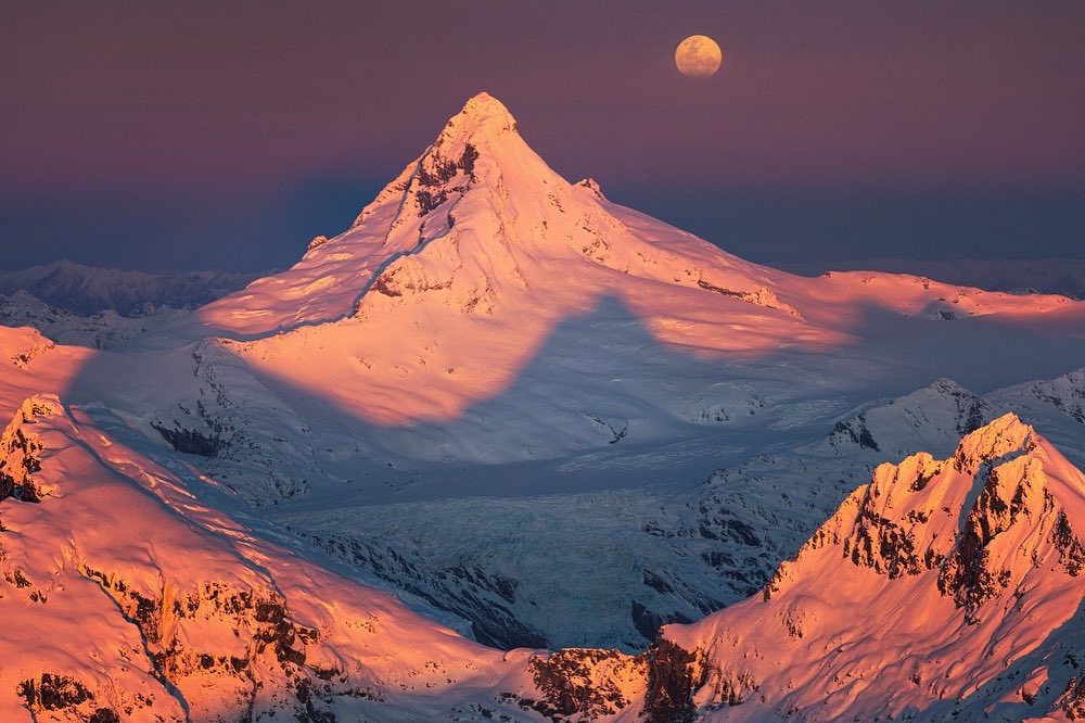 Moon and mountain, ignited by the setting sun.