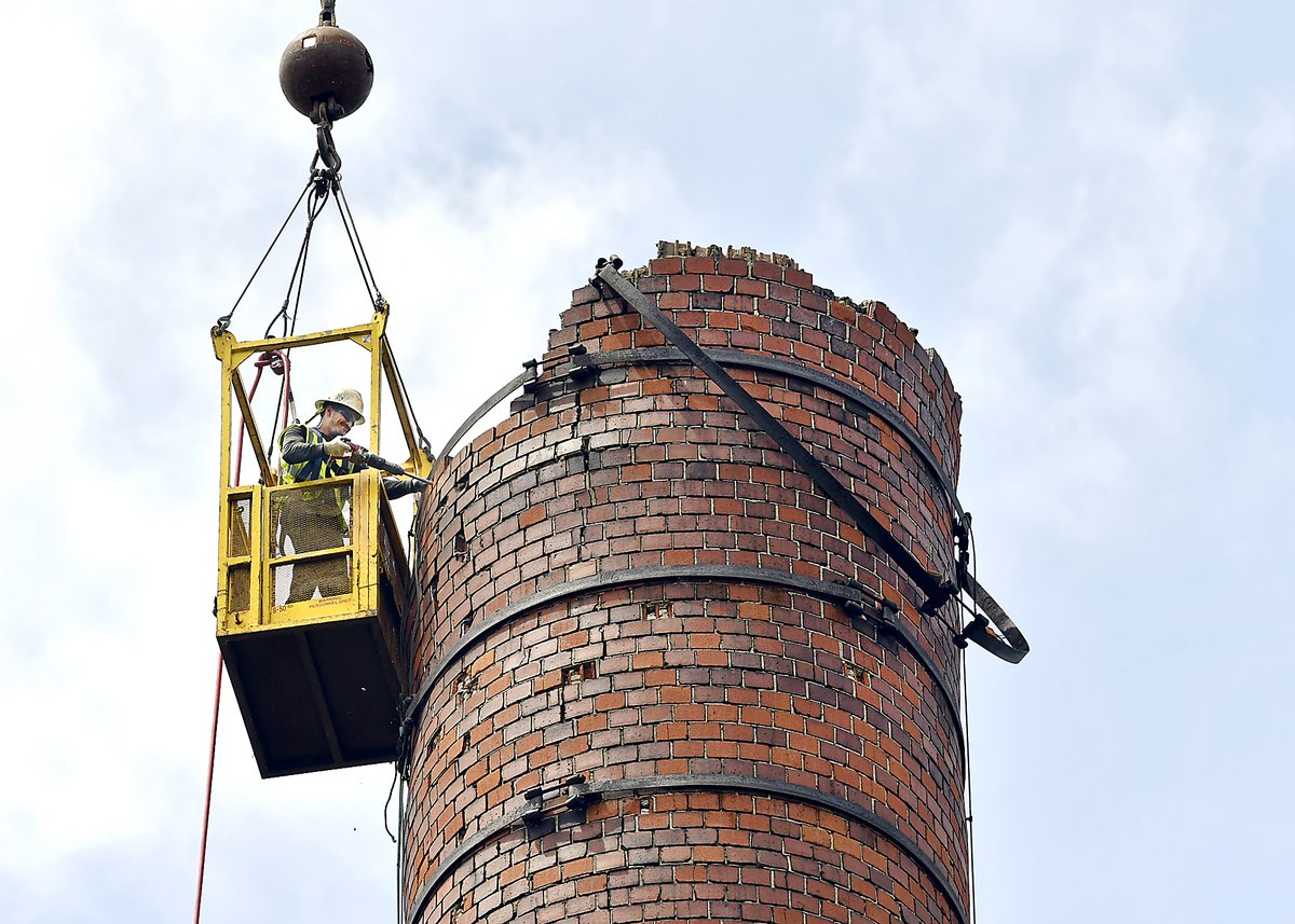 Work began Monday on tearing down the old Nicholson File smokestack. Equipped with an air chisel this worker cuts away the bricks a section at a time while suspended from a large crane. The stack is too unstable to take down any other way except piece-by-piece.