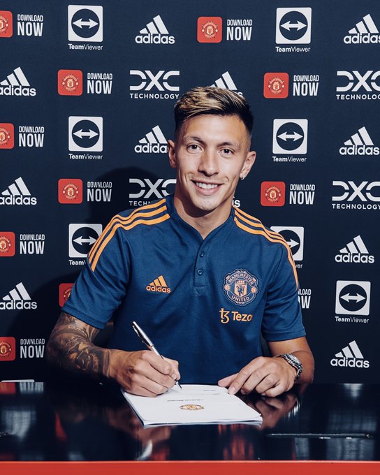 Lisandro Martinez smiles towards the camera as he holds a pen above a United contract. 