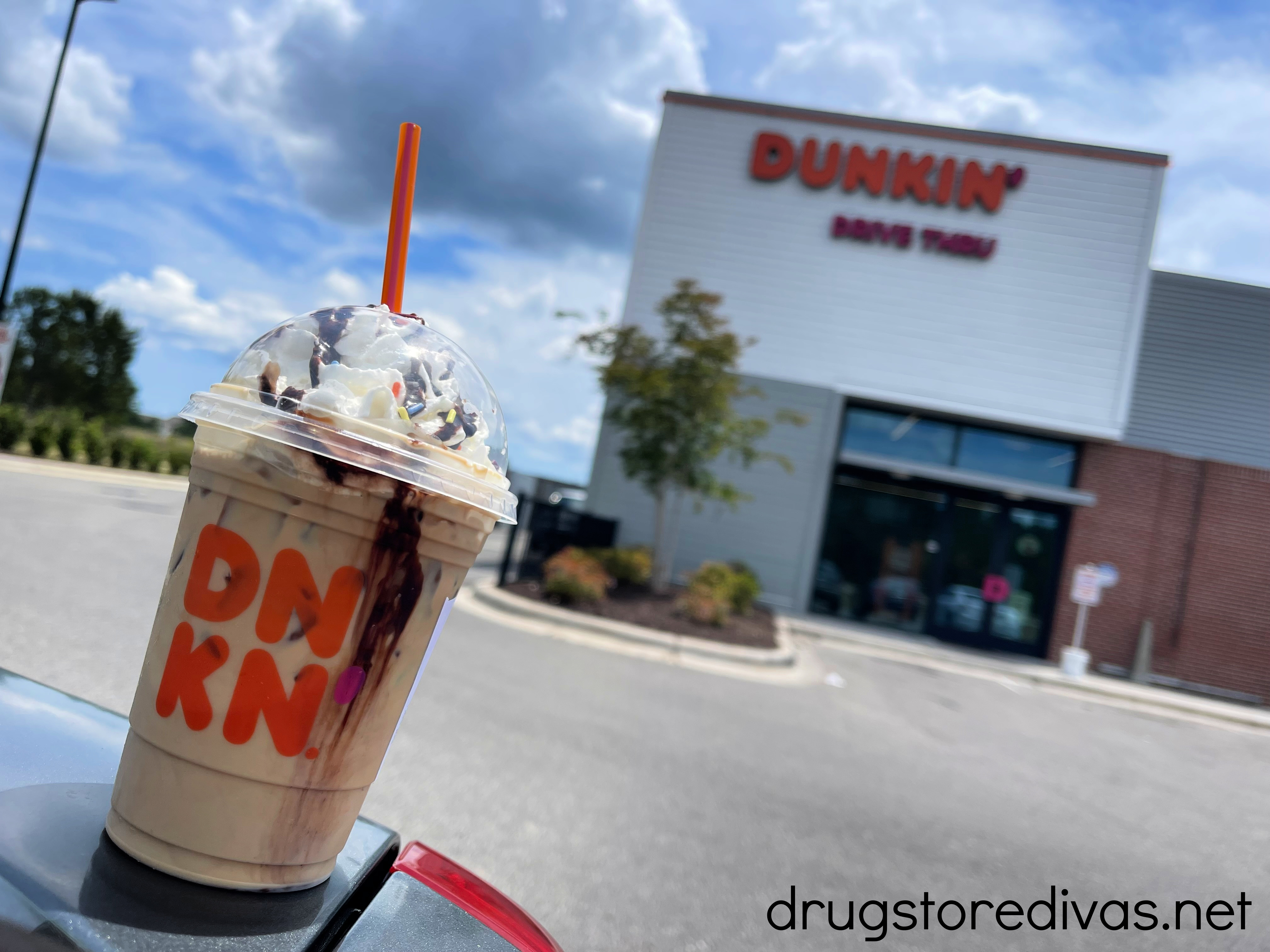 A coffee on a car with a Dunkin' behind it.