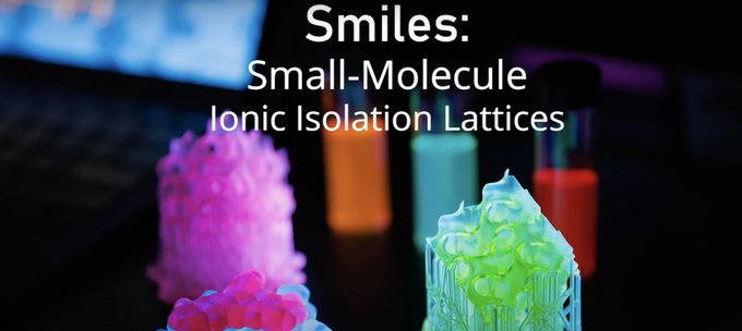 dark background with laptop screen illuminating a keyboard in upper right corner. Text reads Smiles: Small-Molecule Ionic Isolation Lattices with test tubes half full of a glowing liquid below the text. We also see small, fragmented glowing textured bits of a material below the words, on the table.