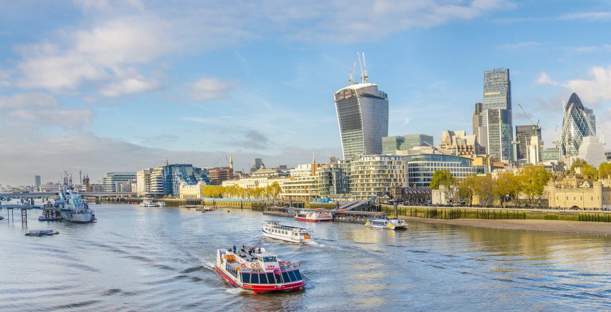 Landscape view of the City of London and River Thames, with multiple boats driving up and down the river. 