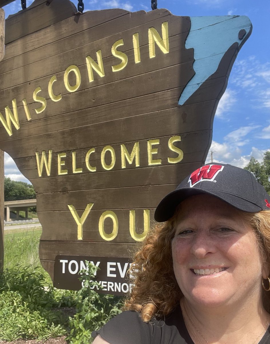 A selfie photo of Chancellor Mnookin standing in front of the “Wisconsin Welcomes You” wooden road sign