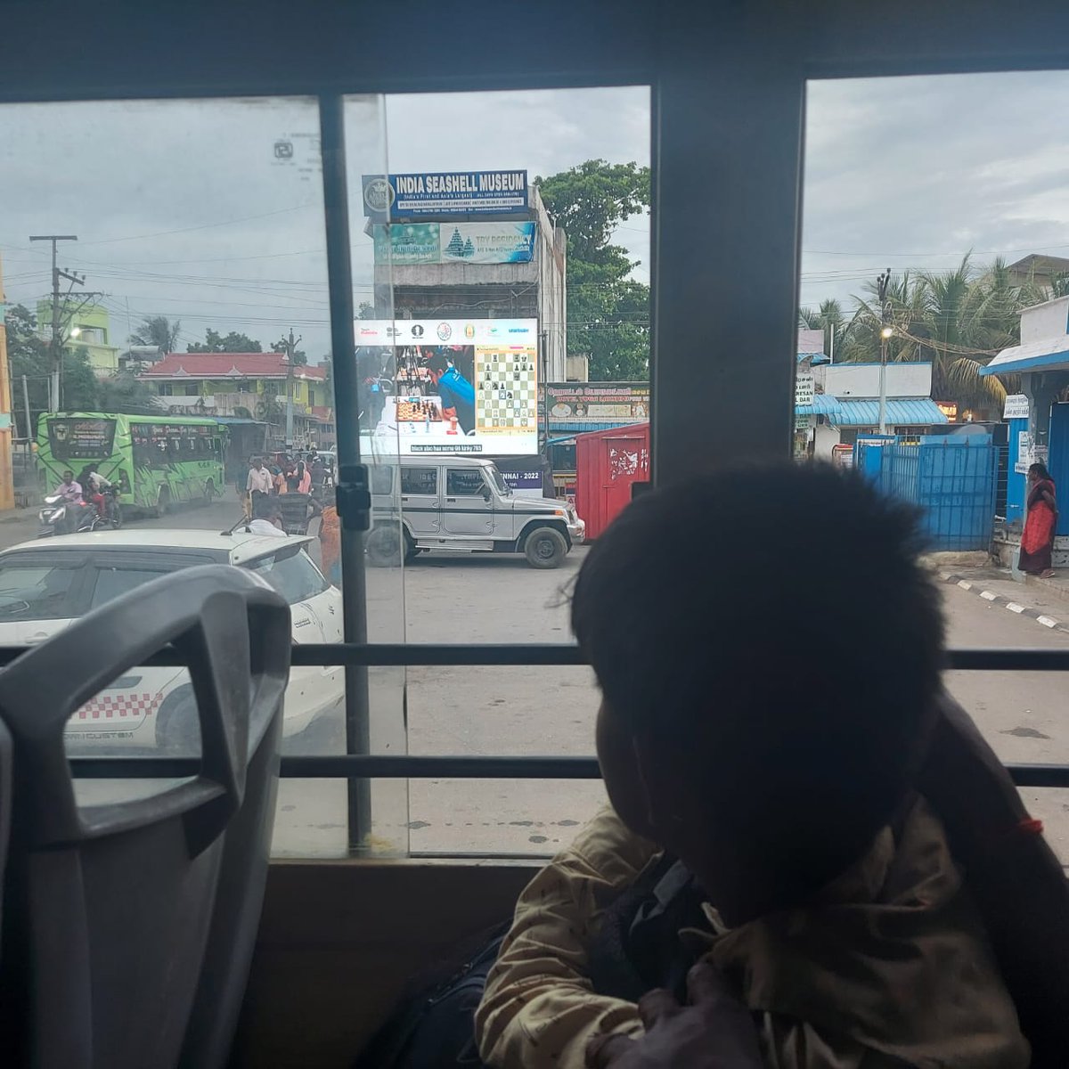 ninansusan's tweet image. A screen showing live chess games at the Mamallapuram bus stand. People stopping to catch a glimpse on a Sunday evening. A kid watches from a parked bus. What a  delightful sight! 

 #ChennaiChess2022 #olympiad2022