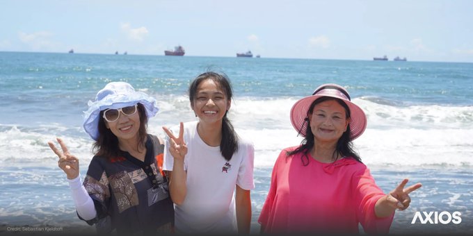 A photo of tourists posing for a photo on the beach near Kaohsiung Harbor as cargo ships anchor outside the Taiwanese port. Photo credit: Sebastian Kjeldtoft.