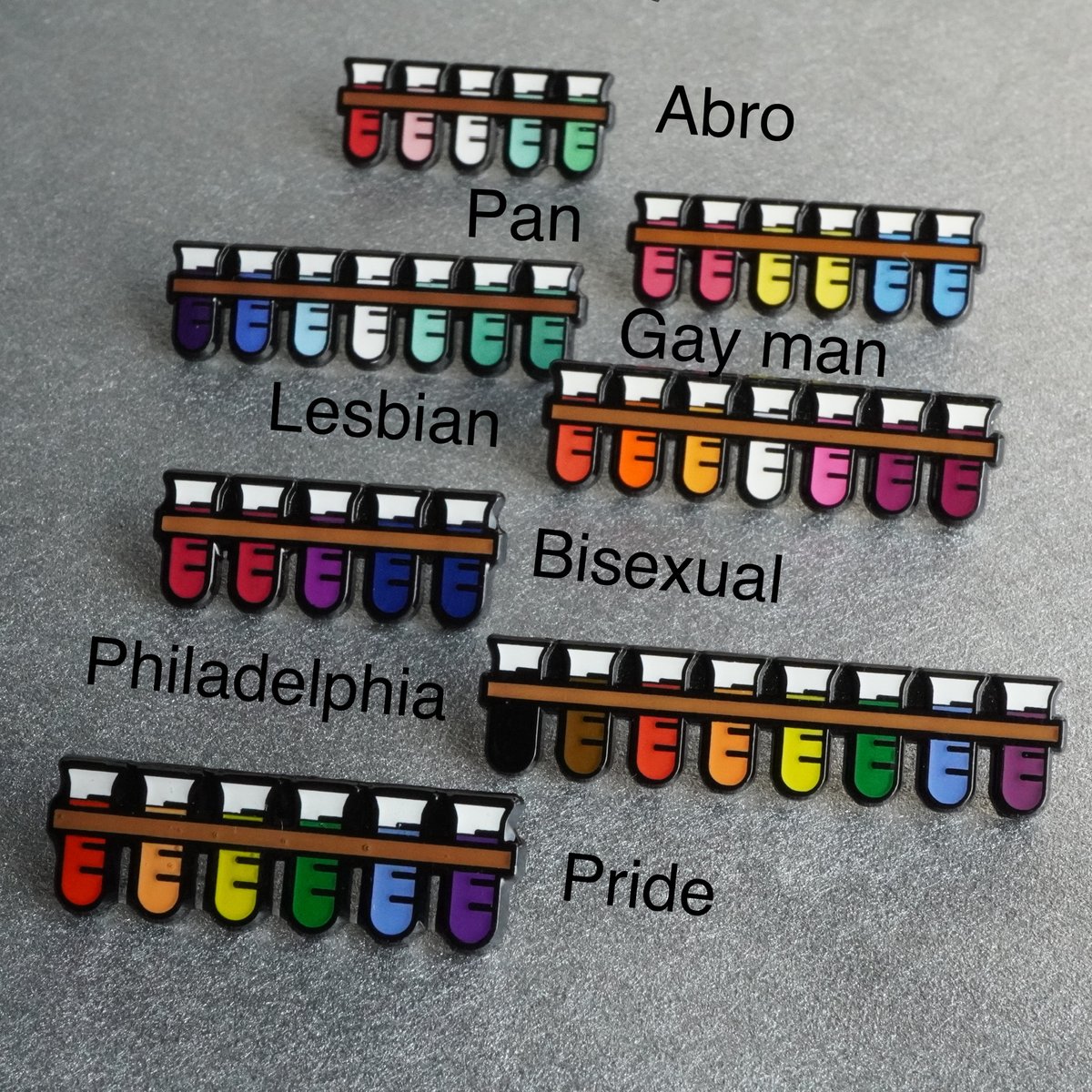 JamieBGall's tweet photo. They're here! 
I've been asked for lots of different identities to be reflected in my pins so I'd like to introduce the whole test tube family. Tell your pals &amp; let's brighten up some lab coats
🖤🤎❤️🧡💛💚💙💜
All profit goes to @aktcharity 
#LGBT #LGBTQ
https://t.co/tWuxfCIlbq https://t.co/iJKeM08g1R