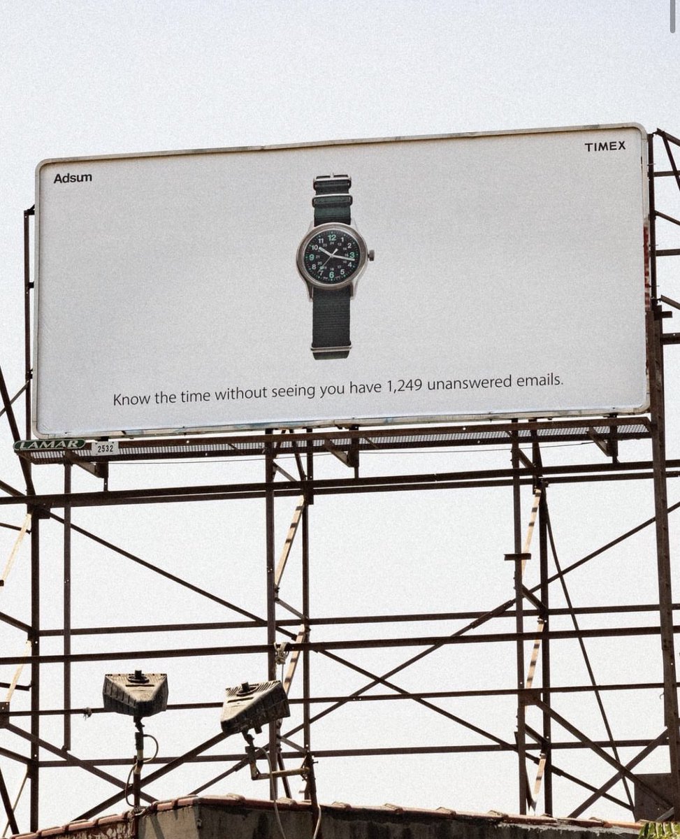 A billboard advertising an analog watch and caption identifying its use for seeing time not emails.