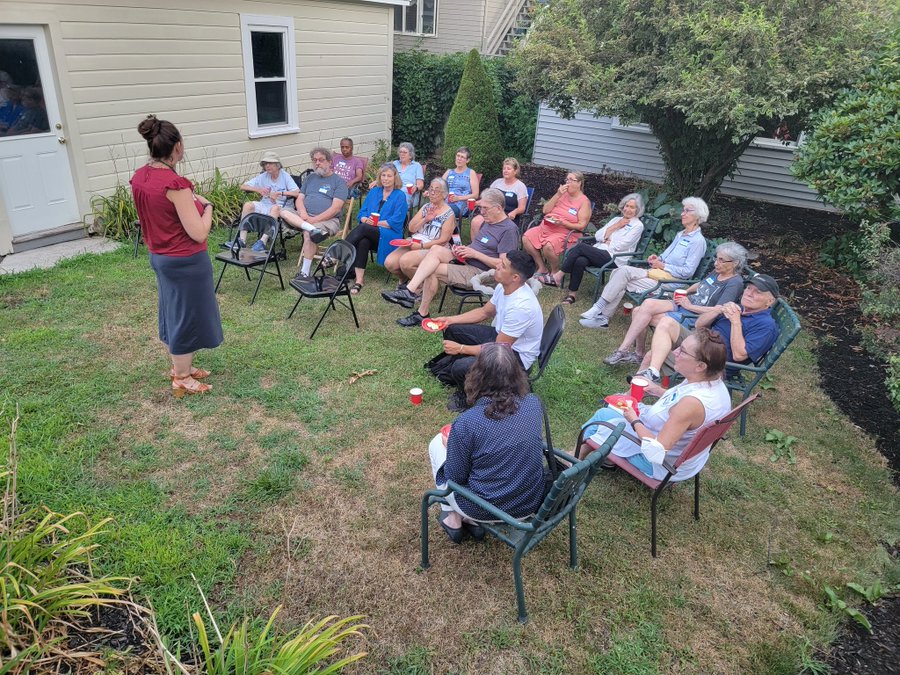 Virginia Leigh speaking with residents sitting in chairs in a grassy backyard in Lynn.