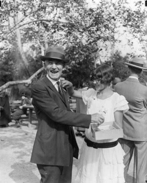 The next #HighlandParkPhoto… Women touching the lapel of a man's suit at a state picnic in Sycamore Grove Park, Highland Park. She is holding a box with things in it. Undated photo #LAPLPhotos #HighlandPark