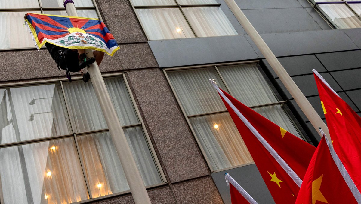 Bold activism outside APEC summit in San Francisco as a demonstrator raises the Free Tibet flag outside the hotel where China's President Xi Jinping meets with U.S. business leaders. powerful visual reminder that voices for freedom and human rights transcend diplomatic corridors.