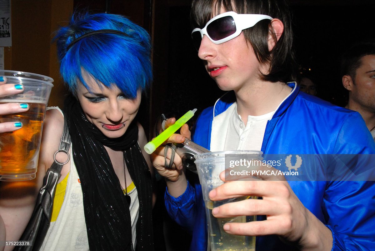 New rave couple, girl with blue hair and boy in electric blue jacket holding a camera and a glowstick, CSS gig (2007)