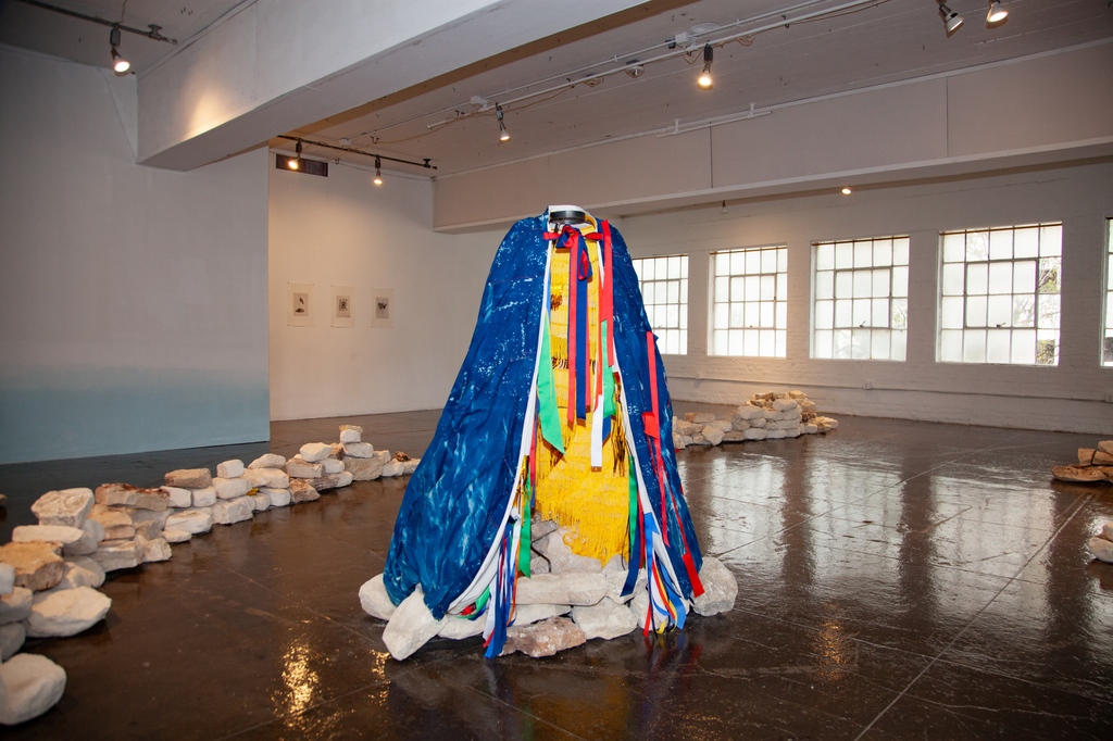In Alexandra Robinson's Artpace exhibition, nestled in the center of a stack of stones stands a figural-like frame draped in a cape created with a cyanotype exterior and ribbons along the interior, titled "After Cōātlīcue."

ℹ️ On view at Artpace through January 7, 2024