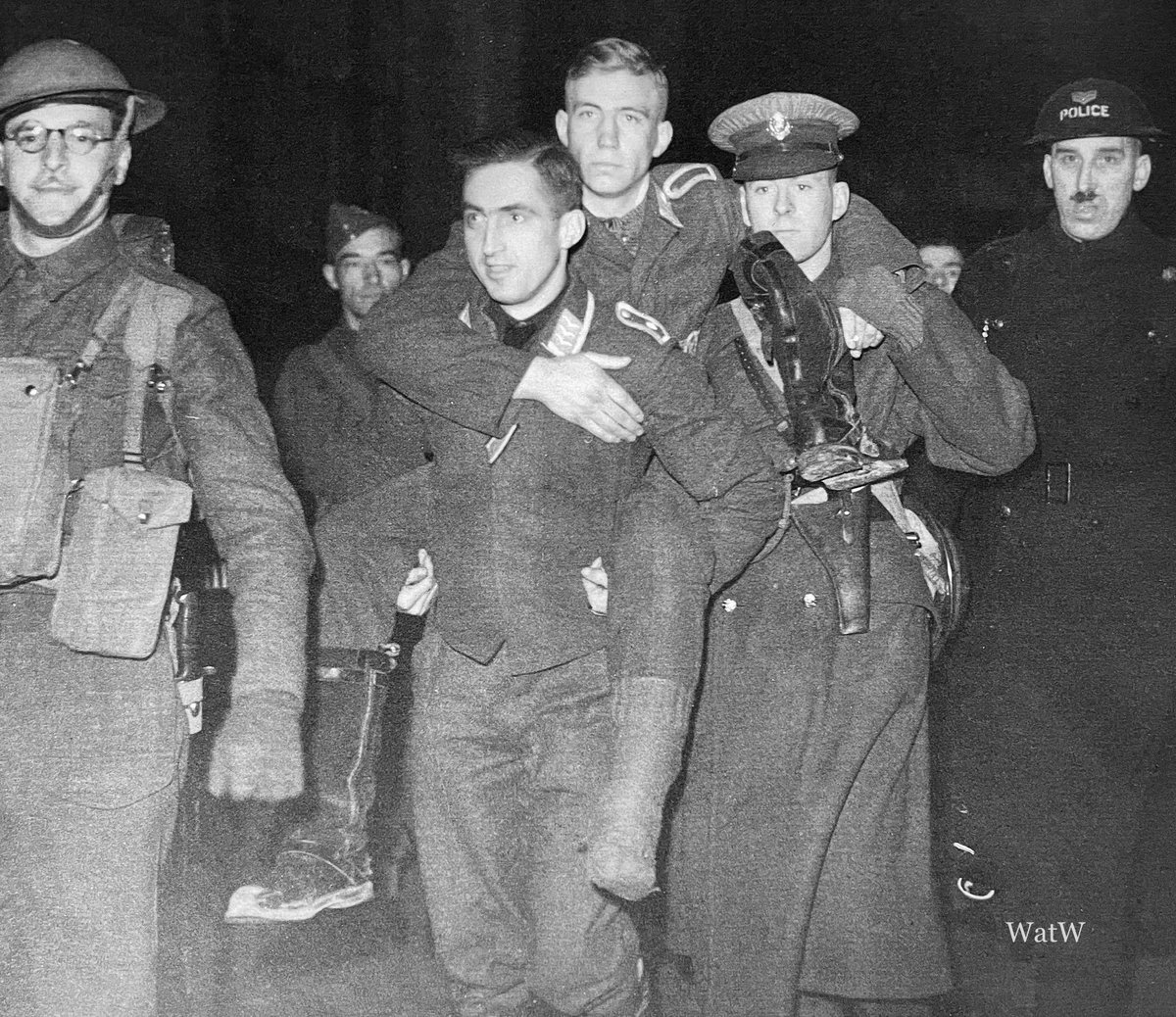 A German airman carries his injured comrade as they are escorted into captivity after being shot down - Manchester, England 1941 #pow #prisonerofwar #manchester #england