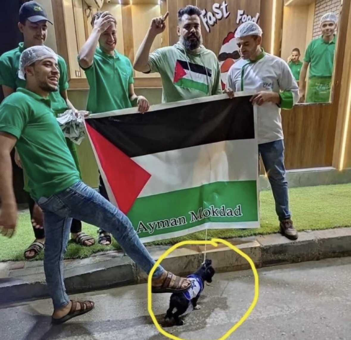 Palestinian supporters step on a puppy wrapped in the Israeli flag. They also attach a zip tie and string around the young puppy’s neck to the Palestinian flag as they smile and laugh.