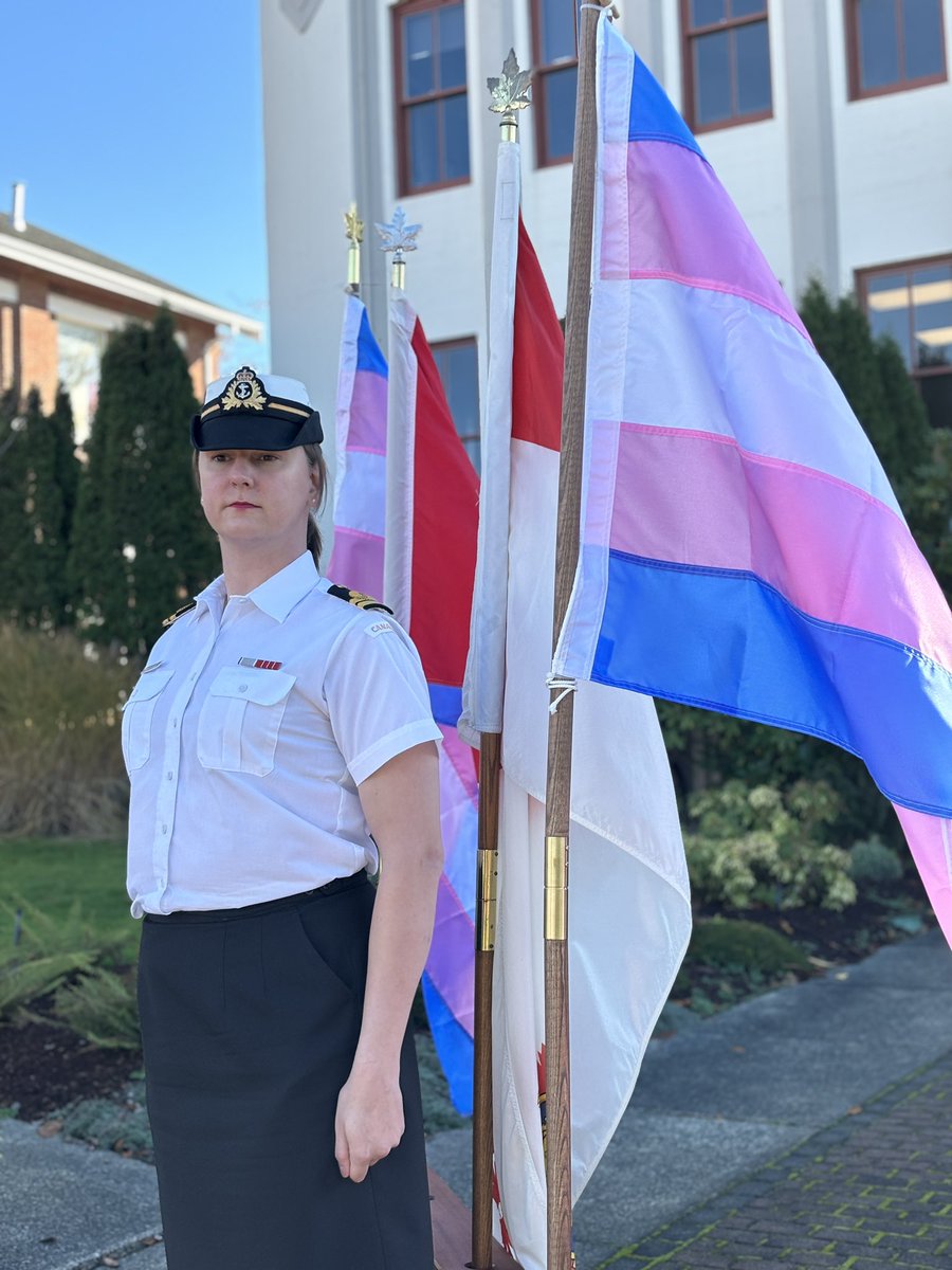 Lieutenant (Navy) Michele Newman, Defence Team Pride Advisory Organization (DTPAO) Military Co-Chair stands beside the Transgender, Canadian Forces and Canadian flags .