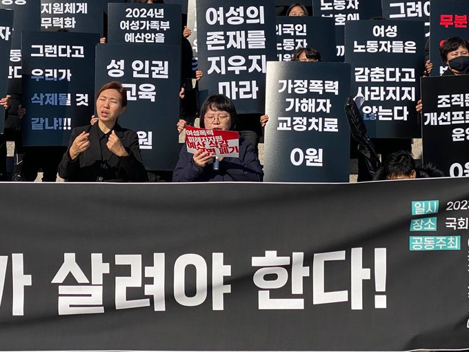 여성폭력 피해자 지원 예산 삭감 전면 폐기라고 적힌 빨간색 피켓을 든 사람이 발언을 하고 있다.
