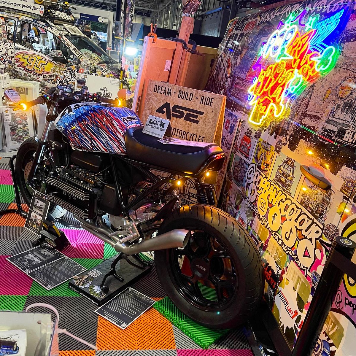 Popbangcolour's tweet photo. The @popbangcolour stand adding a splash of colour to hall 3 @motorcyclelive this week,

The @asecustommc x PBC #Paintwithcars custom BMW K100 on display too. 🏍️+🎨

Prints &amp; merch available on the https://t.co/zcoBbhNaMN 

#MotorcycleLive #motorcyclelive2023 https://t.co/cyhyMy9rny