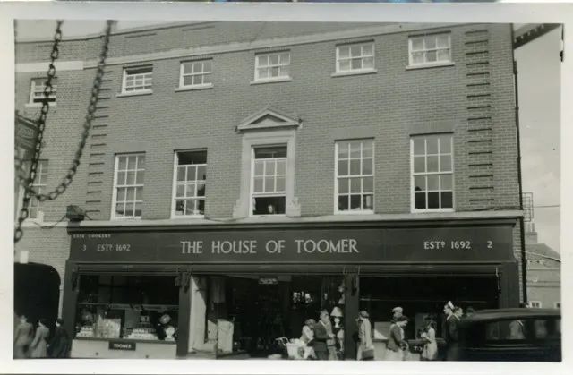 WBerksMuseum's tweet photo. The House of Toomer started as a small ironmonger’s shop in Newbury Market Place in the 1800s, moving to Northbrook Street &amp; finally, as seen in the painting by Jack Barnes, to Bartholomew Street before closing in 1996. Images copyright West Berkshire Museum. #Toomers #Newbury https://t.co/qQAqSBS1S1