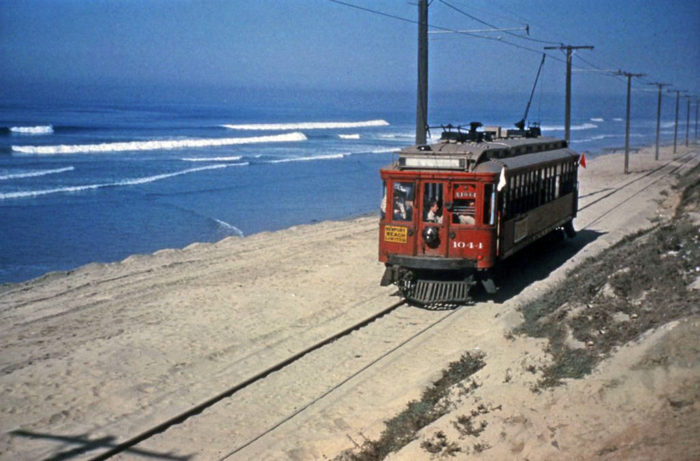 A Pacific Electric red car running near the ocean.