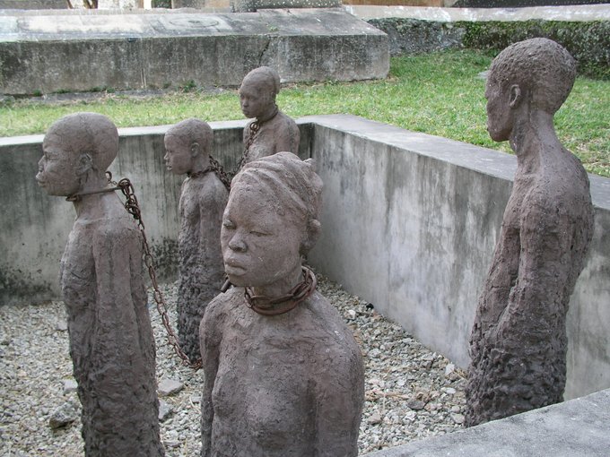 Five stone statues of slaves standing in a pit with chains around their necks.