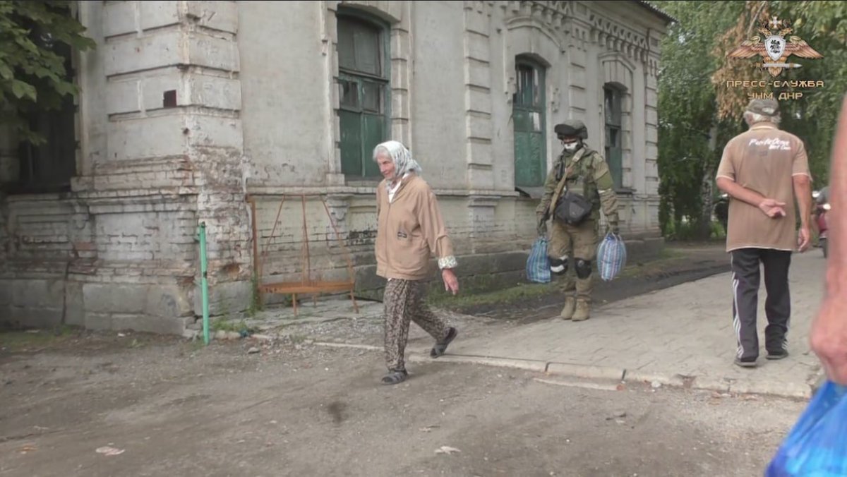 RWApodcast's tweet photo. russian soldier wearing a skull mask carrying groceries for an elderly lady https://t.co/T2qxebPG43