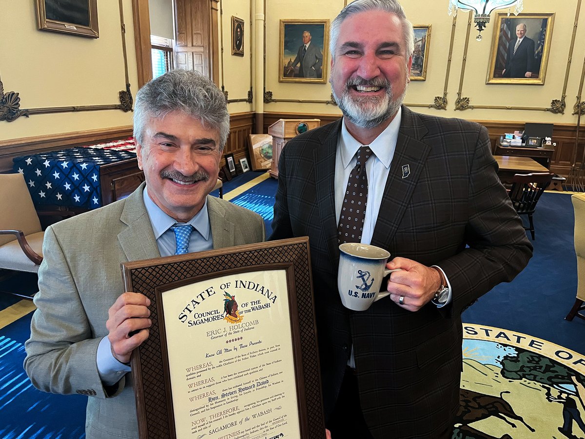 Justice David smiles as he presents his award and Governor Holcomb smiles while holding his U.S. Navy mug.