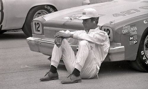The Silver Fox, David Pearson sits resting and relaxing leaning against Bobby Allison,s race car smoking a Winston cigarette would be my best guess! This cat was one cool customer throughout his legendary career!