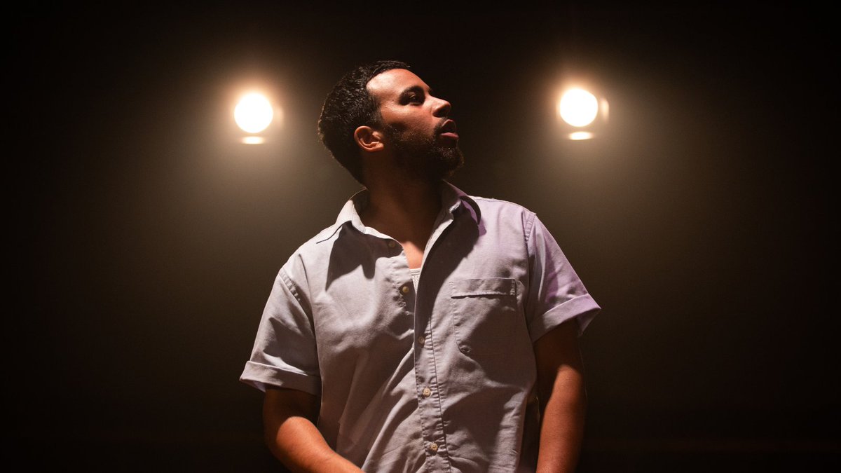 Aaron Anthony stands wearing a button up shirt looks over his shoulder. 