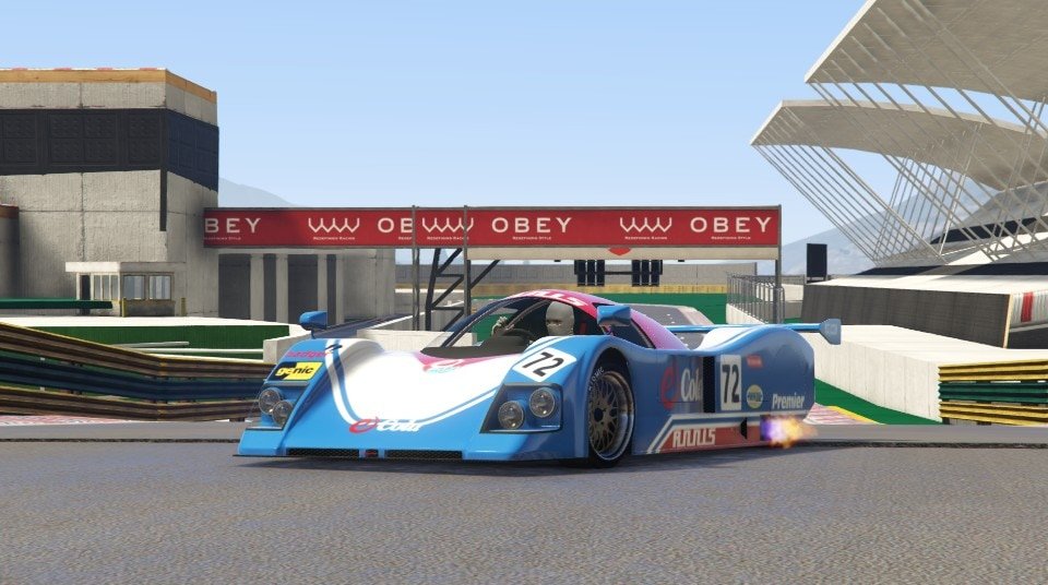 By Pedinhuh on GTAForums.

Depicted is an elegant racing vehicle coloured mostly blue and white, with eCola brand logos. Around it is a race track, with an overhead red Obey brand sign and green and yellow barriers.