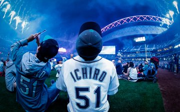 Mariners fans wearing No. 51 Ichiro jerseys look up as blue fireworks light up the sky around the roof of T-Mobile Park.
