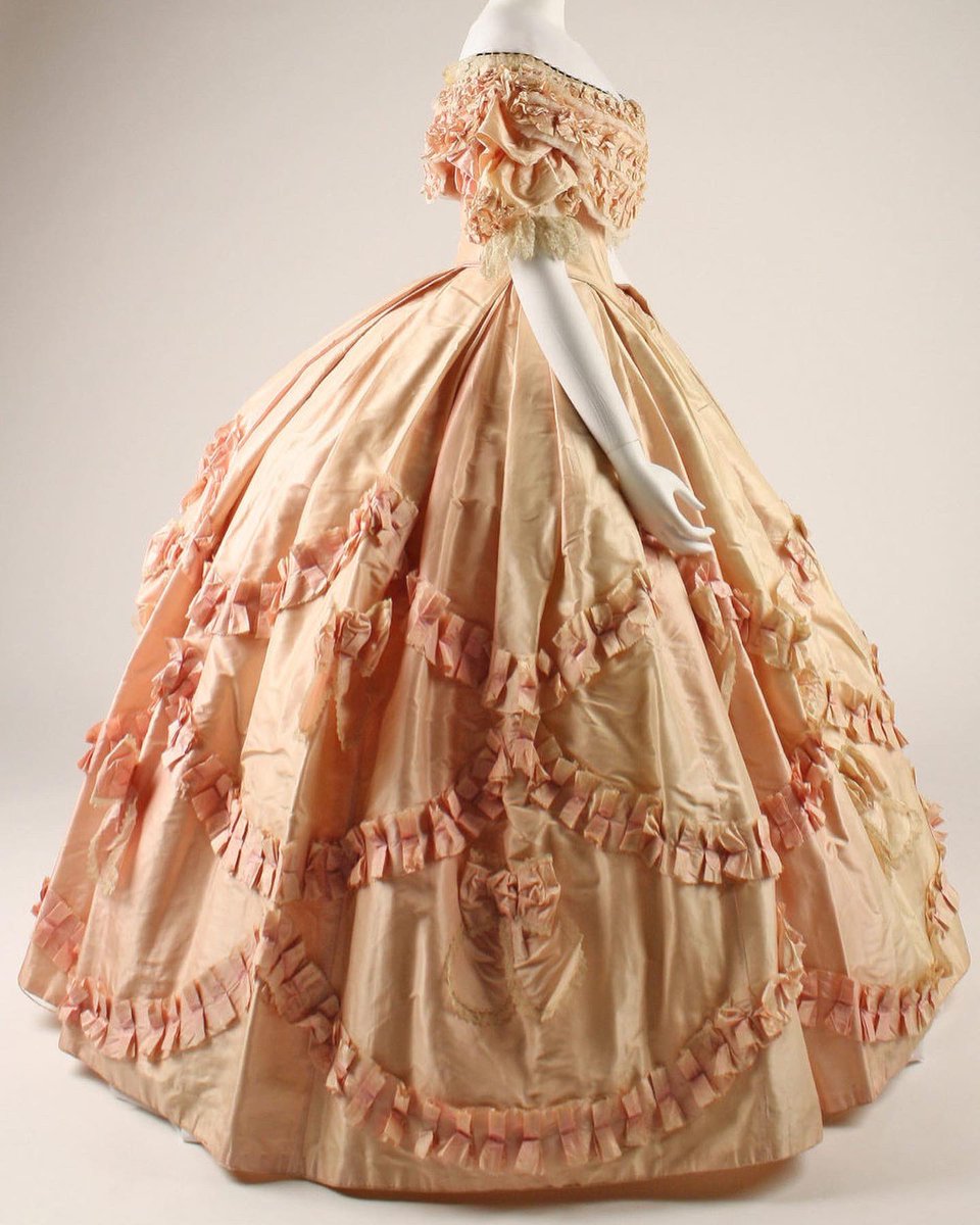 FITfashionstory's tweet photo. This 1860 evening dress is made in a delicate pink silk adorned with simple bows and lace along the bodice and skirt. The bodice of the dress has a wide bertha collar that sits off the shoulder, covering the top half of the arms. Read more!

https://t.co/vMeb9vZQG1 https://t.co/xXP5dssZcA