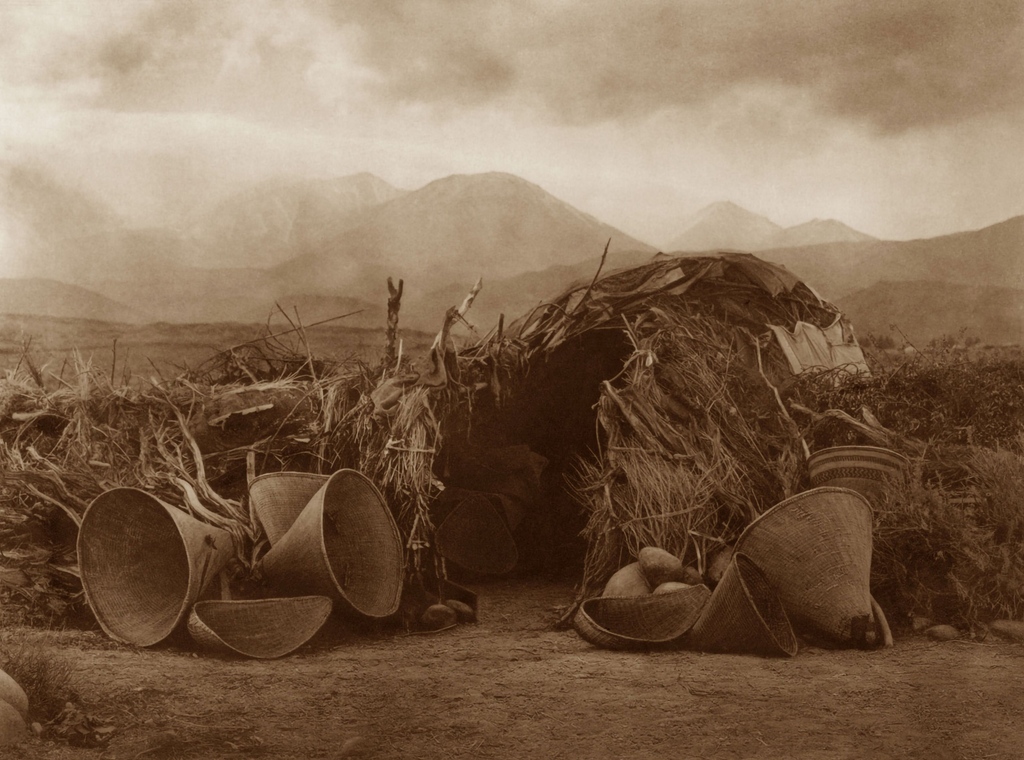 The wikiup is a typical winter shelter and was 12 to 14 ft in diameter. A shallow pit was dug, willow poles set close together around it, bent over and bound at top. Battens were lashed around outside and many courses of dry grass applied.

📸: Edward S. Curtis, A Mono Home, 1924