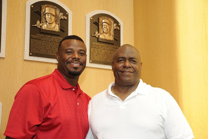 Ken Griffey Jr. (left, wearing red shirt) and Ken Griffey Sr. (right, white shirt) stand in the Hall of Fame Plaque Gallery in front of Ken Griffey Jr.'s plaque. 