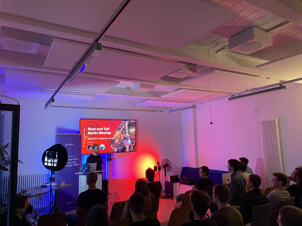 Meetup organizer Basti standing in front of a crowd. Behind him the introduction slide for the Rust and Tell Berlin Meetup.