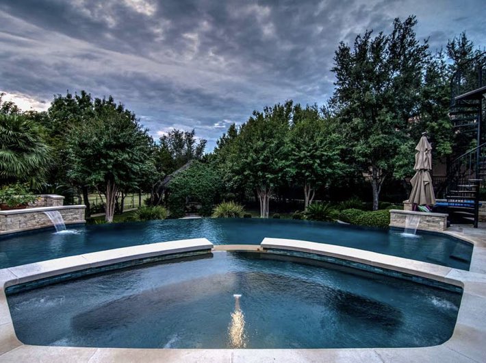 Spillover custom pool surrounded by lush greenery. #AustinPoolBuilders #AustinSwimmingPools #ReliantPools