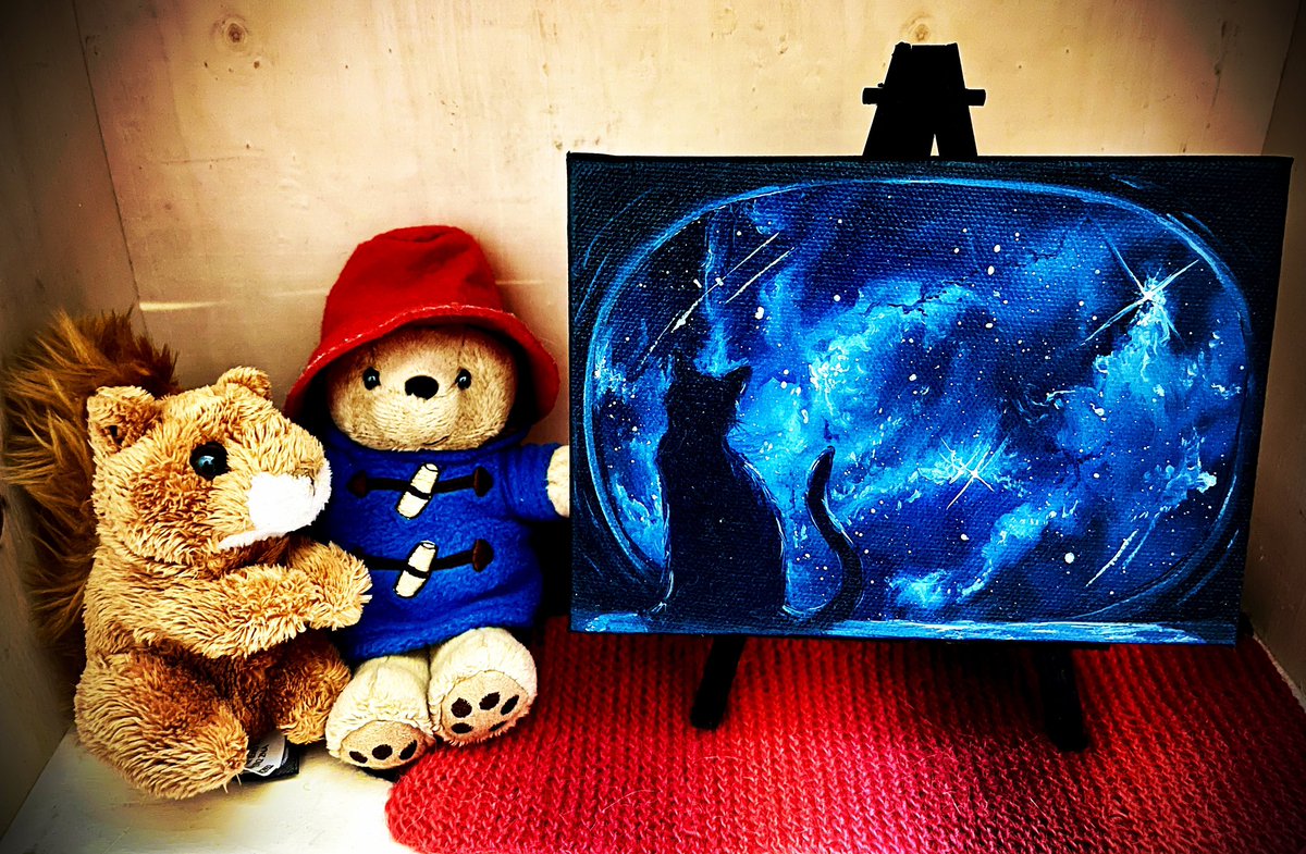 Paddington Bear and Squirrel sit on my knitting, admiring a mesmerizing painting of a cat in space looking out in wonder. etsy.com/shop/ScenesbyC…