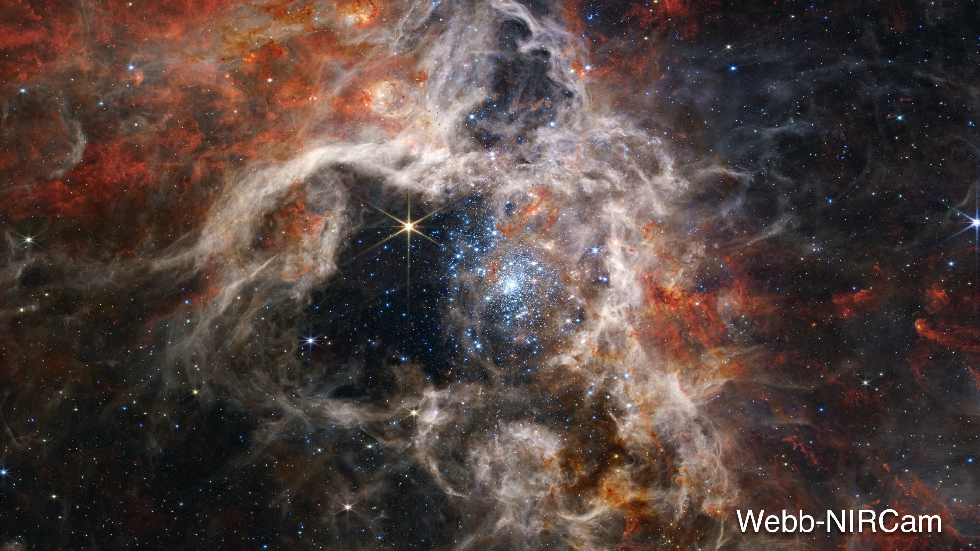 Fluffy tan-colored nebula clouds, with rust-colored highlights, surround a black central area. Within that area, the focal point of the image is one large yellow star with eight long thin points. To the right of this star is a bright star cluster in an oval shape. The stars within the cluster look like tiny pale blue sparkles. The cluster is more densely packed at its core and scatters outward. Towards the bottom of the image, multiple arms appear to spiral out of a cloudy tan knob. Taken together, the structures resemble a spider or a squid. Other blue and yellow eight-pointed stars, as well as distant galaxies, are dotted throughout the image. Credits: NASA, ESA, CSA, STScI, Webb ERO Production Team