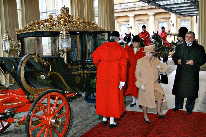 Lula e a rainha Elizabeth II caminham. Foto mostra também carruagem real e guardas da rainha.