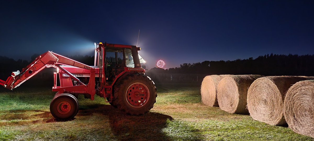Stacking bales with fireworks in background.