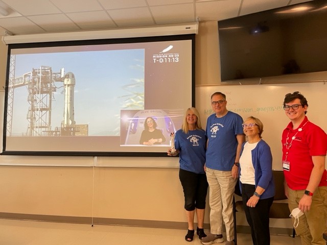 Dr. Kerrie McDaniel , Tyler Rico, Liam Seymore, & Dr. Julia Roberts pose with a replica of their payload attached to the #BlueOrgin launch on #NS23 #wkubiology #NSSP #STEM #mallownauts