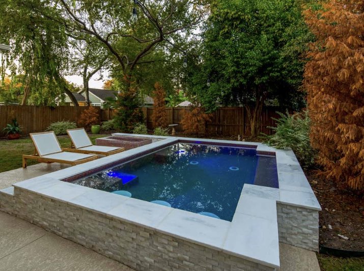 A geometric custom pool goes perfectly in this backyard surrounded by greenery. #AustinPoolBuilders #AustinSwimmingPools #ReliantPools