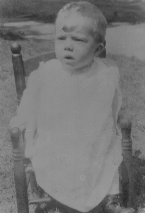 B&W pic of President Carter in 1925 at one year old.  He is wearign a white bib that is covering most of him while sitting in a small wooden chair.