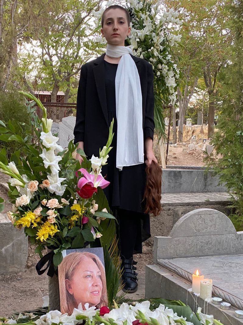 Iconic image of the daughter of Minoo Majidi, the women who was shot dead in protests in Kermanshah last week, standing at her mom’s grave with her own hair in hand. Iranian women have been cutting their hair as a sign of grief and resistance. #MahsaAmini 
(Via @FarahmandAlipur)