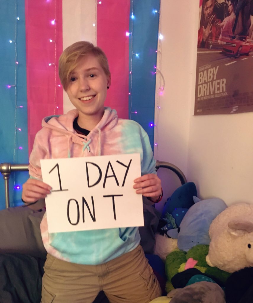 a white, blond trans boy with a squishy face and a sign saying “1 day on T”