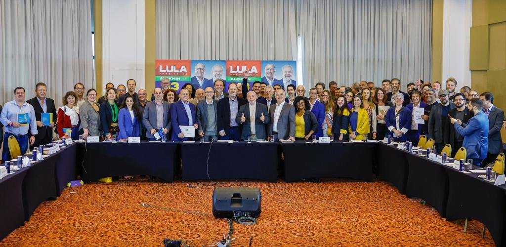Representantes do turismo se reúnem com Lula. Eles posam para a foto, atrás da mesa de reunião. Lula aparece no centro.