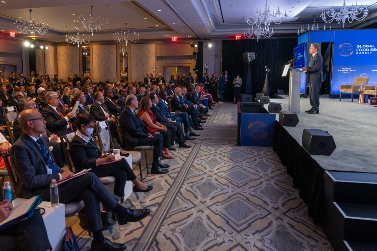 Secretary Blinken speaking from a podium on a stage. A large crowd is seated in front of him. 