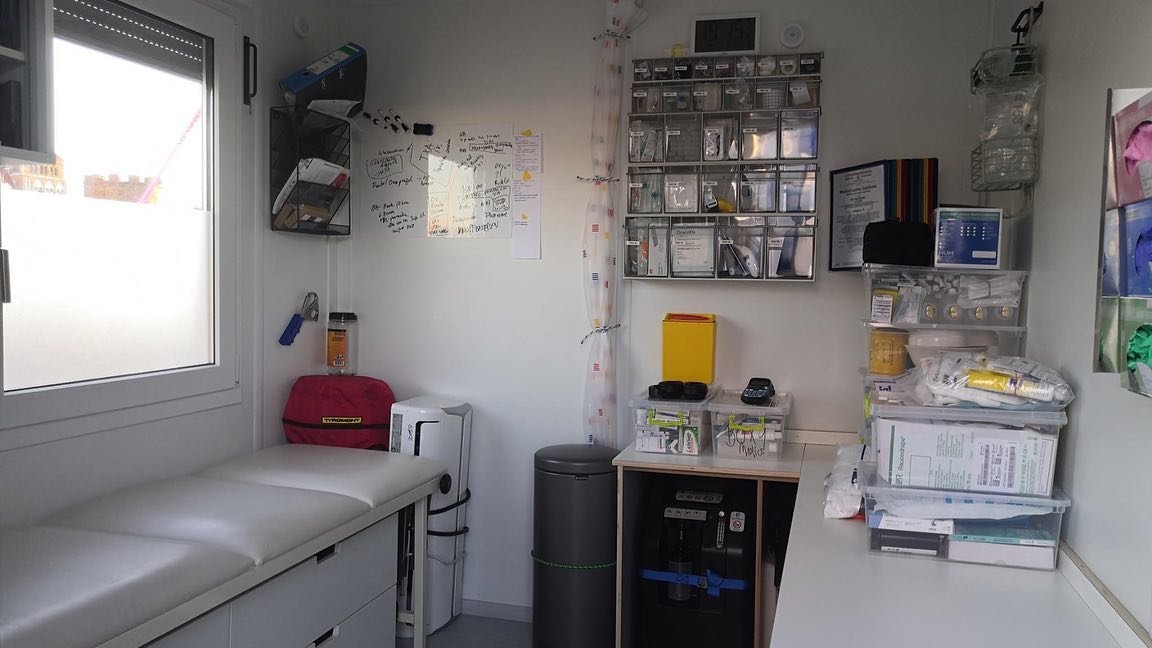 Blick in den Medic-Conatiner. Links eine Behandlungsliege. Verbandsmaterial in ein Regal an der Wand sortiert. Medizinische Geräte.