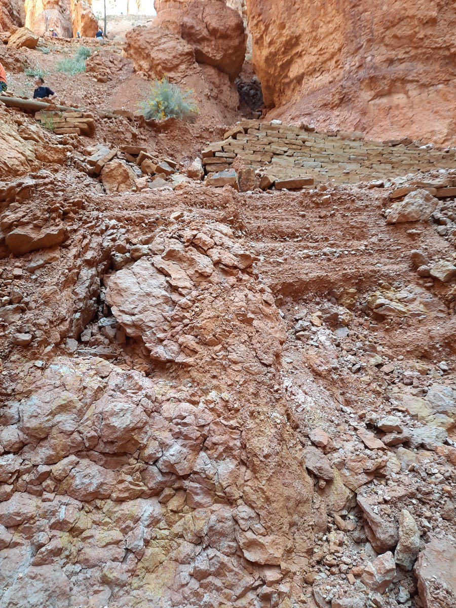 Rock debris and collapsed retraining walls along red rock canyon trail after flooding event.