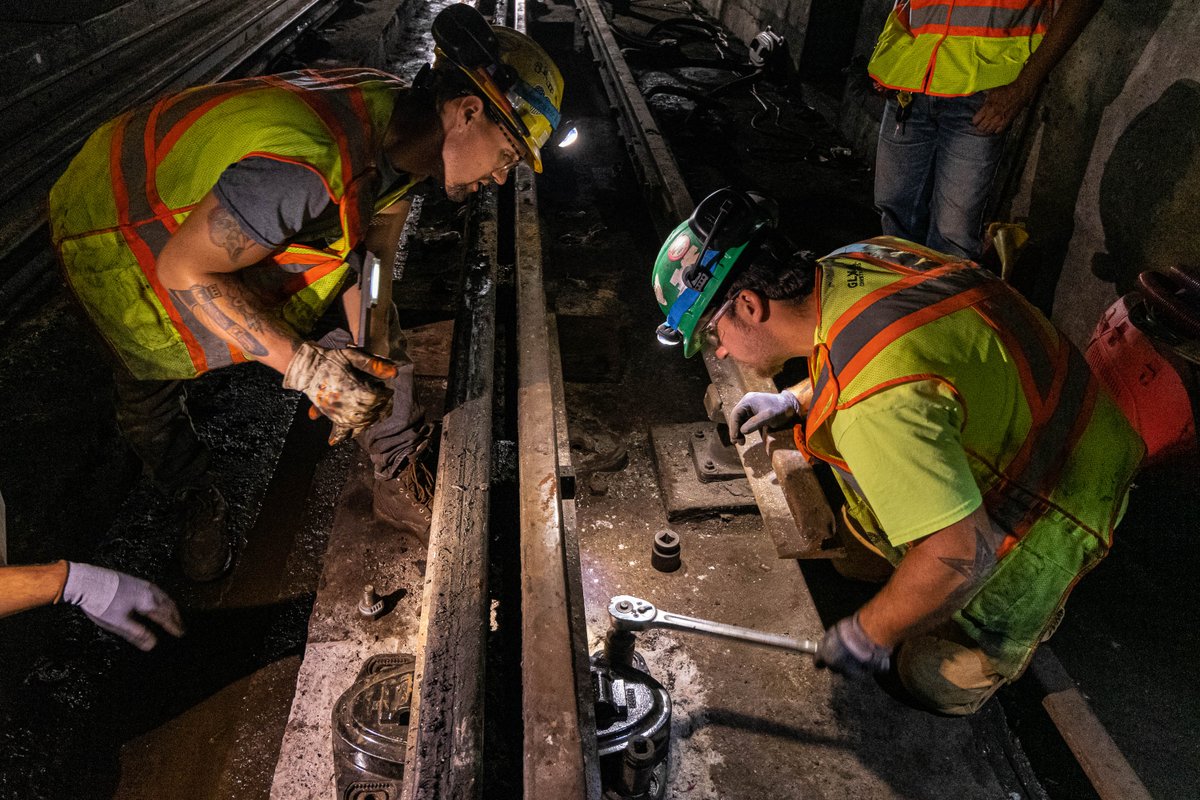 Track workers in yellow safety vests and hard hats working on Cologne eggs - special rail fasteners - in the tunnel under Tufts Medical Center.